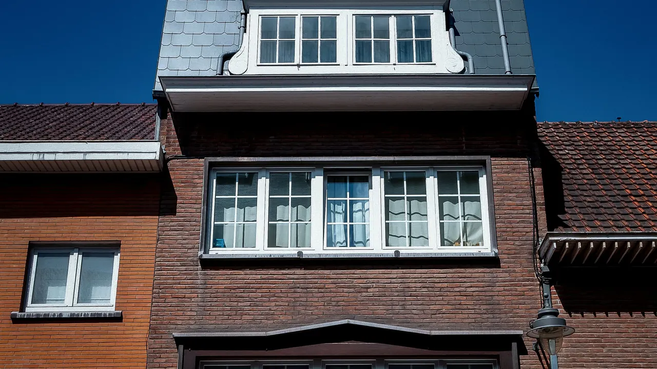 Maison en brique aux châssis blancs et à la lucarne en ardoise sous un ciel bleu