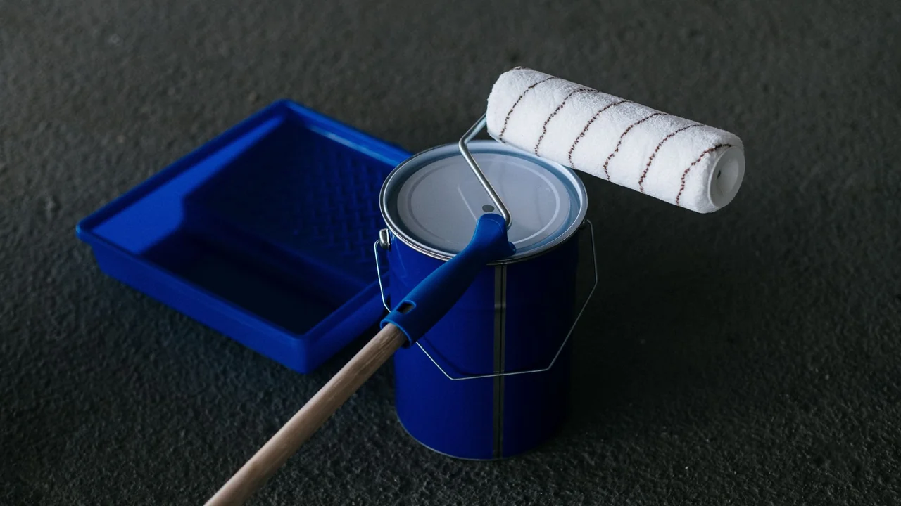 Pot de peinture, rouleau et bac bleus posés sur un sol sombre